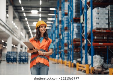 A woman warehouse inspector wearing a hard hat and safety jacket smiles broadly as they hold a clipboard. The brightly lit storage space highlights the precision of the warehouse arrangement. - Powered by Shutterstock