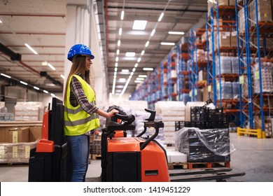 Woman Warehouse Worker Operating Forklift Machine In Large Distribution Warehouse Center. Manual Worker Relocating Goods In Factory Storage Area.