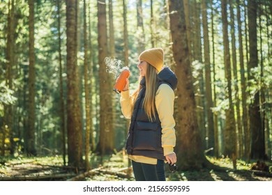 Woman in warm clothes drinking tea enjoys a walk in a pine forest