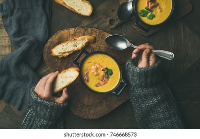 Woman In Warm Grey Sweater Eating Corn Creamy Chowder Soup With Prawns Served In Individual Pots, Top View. Woman' S Hand Keeping Spoon And Bread Slice. Flat-lay Of Rustic Dinner Table. Slow Food