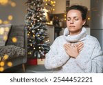 Woman in a warm knit sweater meditating and practicing breathing exercises at home during Christmas holidays, with a Christmas tree in the background.