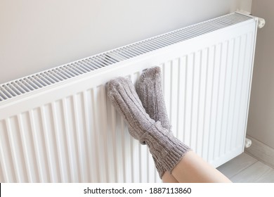 Woman Is Warm Knitted Woolen Socks Near A Home Heater In Cold Winter Time. Using Heater At Home In Winter.