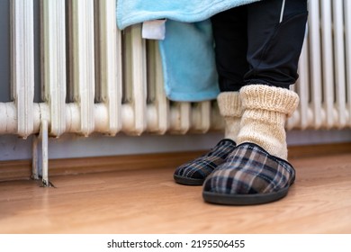 Woman In Warm Knitted Woolen Socks Near A Home Heater In Cold Winter Time. The Symbolic Image Of The Heating Season At Home. Part Of Body, Selective Focus. Electric Or Gas Heater At Home