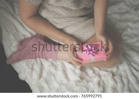 Woman in warm knitted woolen socks at cozy home atmosphere on the bed. Young woman with a Christmas gift in hands enjoying free time with comfort. Soft light and comfy lifestyle concept. Top view.