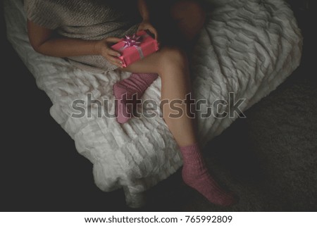 Woman in warm knitted woolen socks at cozy home atmosphere on the bed. Young woman with a Christmas gift in hands enjoying free time with comfort. Soft light and comfy lifestyle concept. Top view.