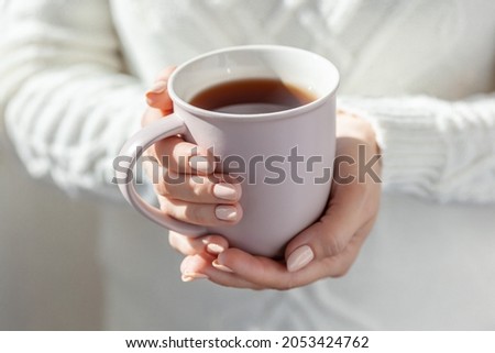 A woman in a warm white sweater holds a mug in her hands. Close-up of female hands holding a cup of coffee or tea