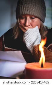 Woman With Warm Winter Clothes Is Is Reading Indoors A Letter Or Bill In The Candlelight