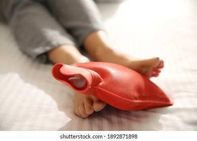 Woman Warming Feet With Hot Water Bottle On Bed, Closeup