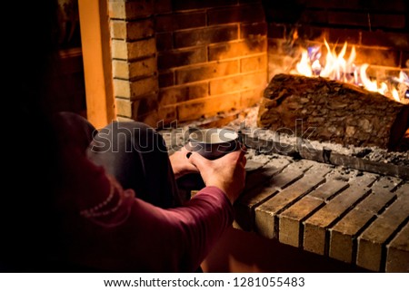 woman is warming in a fireplace while she is drinking coffee