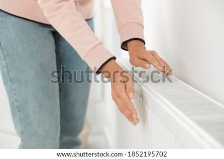 Woman warming hands on heating radiator near white wall, closeup