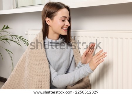 Woman warming hands on white heating radiator indoors