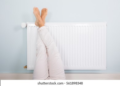 Woman Warming Up Her Feet On White Radiator At Home