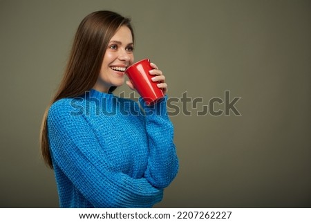 Woman warming with hot drink. Isolated portrait of girl drinking from red glass and looking away.