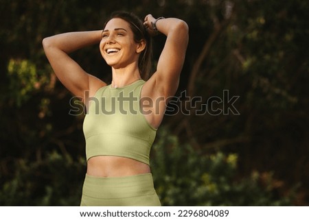 Woman warming up for a morning workout outdoors. Happy sports woman tying her hair and preparing for yoga. Fit woman standing against a nature background. Stock foto © 