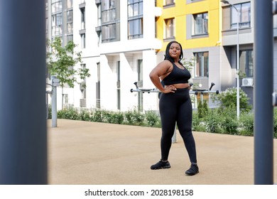 Woman Warming Up Muscles Before Running Jogging In City Outdoors, Side View On African Obese Overweight Lady In Black Tracksuit Engaged In Workout. Sport, Activity, Healthy Lifestyle And Weight Loss