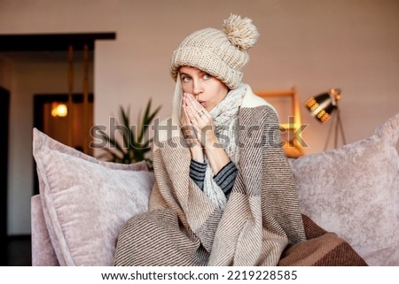Woman warmly clothed and hat in a cold home sitting on couch. Saving energy resources