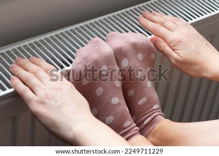 A woman warms her feet and hands in socks on a radiator. Home heating. Low temperature and cold in the house. Photo closeup