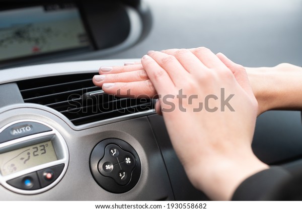 The woman warms her hands over the car\'s hot air\
outlet. Cold hands.