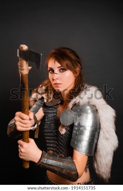Woman warrior in chain mail armor with
lamellar bracers and plate shoulder pad with the fur of a polar fox
on her shoulders, stands in a fighting stance with an ax in her
hands against dark
background