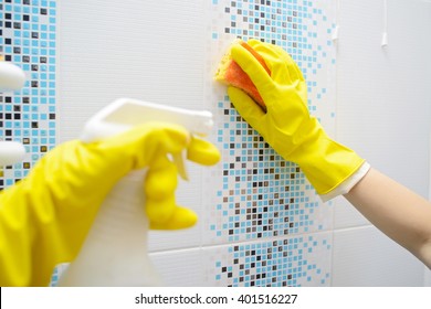 A Woman Washer Is Cleaning Tiled Surface In Bathroom. The Girl Is Holding A Cleaning Spray And A Sponge In His Hands. Copy Space