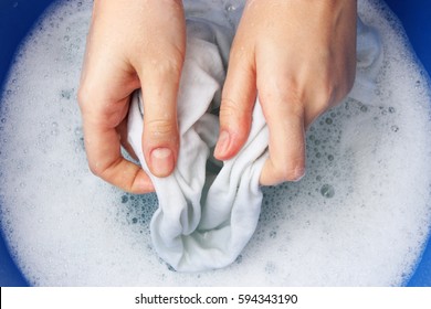 A Woman Washes Clothes By Hand In Soapy Water.