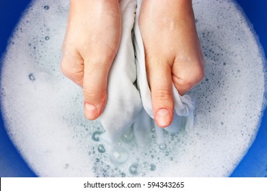 A Woman Washes Clothes By Hand In Soapy Water.