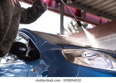 A woman washes her dirty car in the car wash. - Shutterstock ID 1930054532