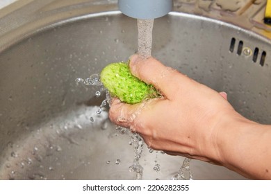 A Woman Washes A Ripe Cucumber Under Running Water In The Sink In The Kitchen