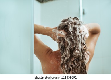 Woman washing away shampoo in shower. Rear view
