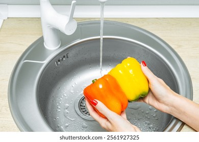 woman washing bell peppers in kitchen sink. housewife washes vegetables in the kitchen. bell pepper in the kitchen. woman holding bell peppers in her hands.  - Powered by Shutterstock