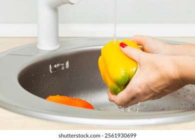 woman washing bell peppers in kitchen sink. housewife washes vegetables in the kitchen. bell pepper in the kitchen. yellow bell pepper. High quality photo - Powered by Shutterstock