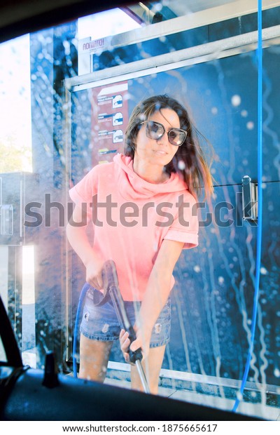Woman washing car with pressure washer
at self-service car wash station, view from the
car