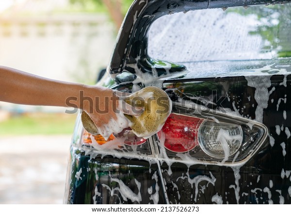 Woman washing car tail lights with shampoo at\
home. Car detailing\
concept.