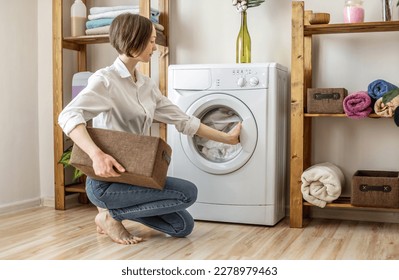 A woman is washing clothes in a washing machine in a laundry room. The concept of caring for things, cleaning and hygiene - Powered by Shutterstock