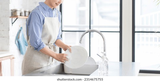 A woman is washing the dishes in the kitchen and running bubbles with water. - Powered by Shutterstock