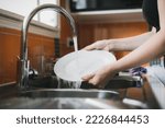 Woman washing dishes in kitchen sink, close up of hands rinsing plate.