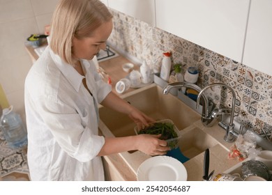 A woman is washing fresh greens in a modern kitchen, preparing healthy snacks for school. The scene embodies care, health, and the daily routine of meal preparation. - Powered by Shutterstock