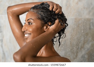 Woman washing hair showering in bathroom at home. Smiling black woman bathing while looking away. Happy woman rinsing hair while taking a shower at luxury spa. - Shutterstock ID 1559872667