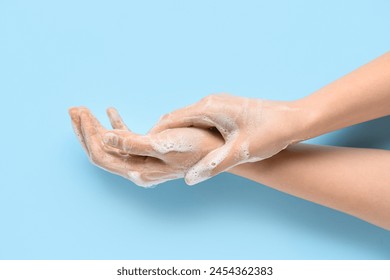 Woman washing hands with soap on blue background