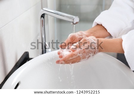 Woman washing hands with soap over sink in bathroom, closeup