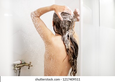 Woman washing her beautiful hair with shampoo standing back in the white shower cabin