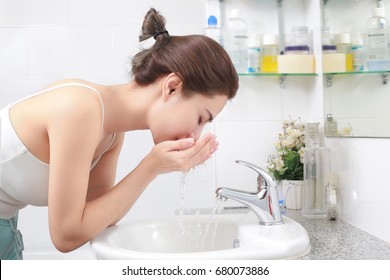 Woman Washing Her Face With Water Above Bathroom Sink.