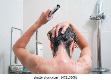 Woman washing her hair with a lot of foam inside a shower. Back view of young woman washing her hair. Woman washes her hair with shampoo in bathroom.