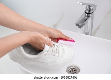 Woman washing shoe with brush under tap water in sink, closeup