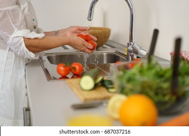 Woman washing tomatoes for salad under tap water to make vegetable salad - Powered by Shutterstock