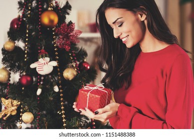 Woman Watch At Christmas Present. Portrait Of Young Female. Preparations For Celebration. Happiness At Home. Profile View. Holiday Concept. Caucasian Young Woman. Decorating Christmas Tree.