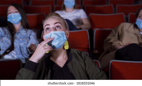 Woman Watches Movie In Protective Mask. Media. Beautiful Young Woman Watches Movie With Interest In Movie Theater. Going To Cinema During Coronavirus Pandemic