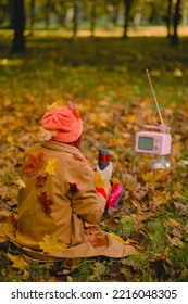 Woman Watches A Small Retro TV On The Park. Autumn Outdoor Recreation. Concept