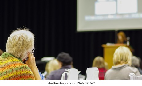 Woman Watching Keynote Speaker At A Conference With A Slide Deck Presentation Projected