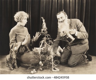 Woman Watching Man In Fake Beard Watering Christmas Tree